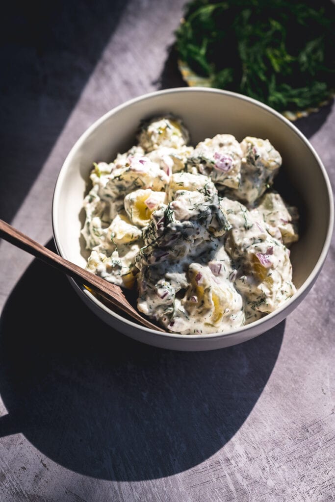 harsh sun light strikes a large white bowl of dill potato salad