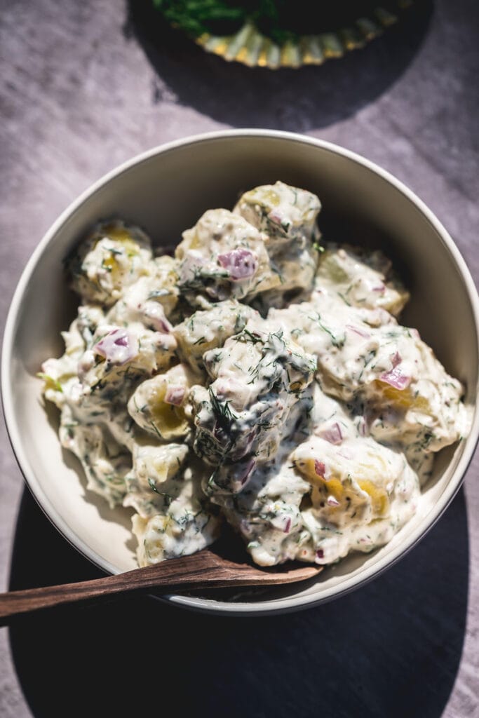 a mound of creamy vegan potato salad rests in a white ceramic bowl