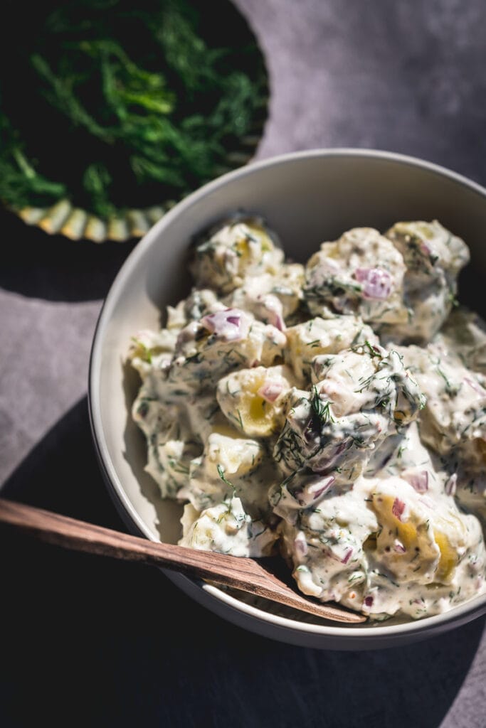 a close up shot of a mound of dill potato salad in a white bowl