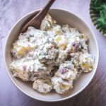 a white bowl filled with creamy dill potato salad with wooden spoon