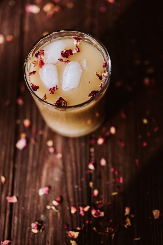 a close up shot of ice and rose petals floating in rooibos tea