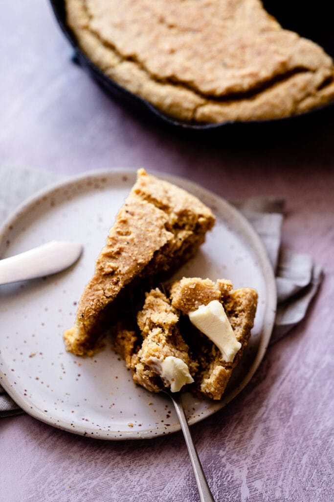 a cast iron skillet gluten free cornbread topped with butter with a fork slicing into it