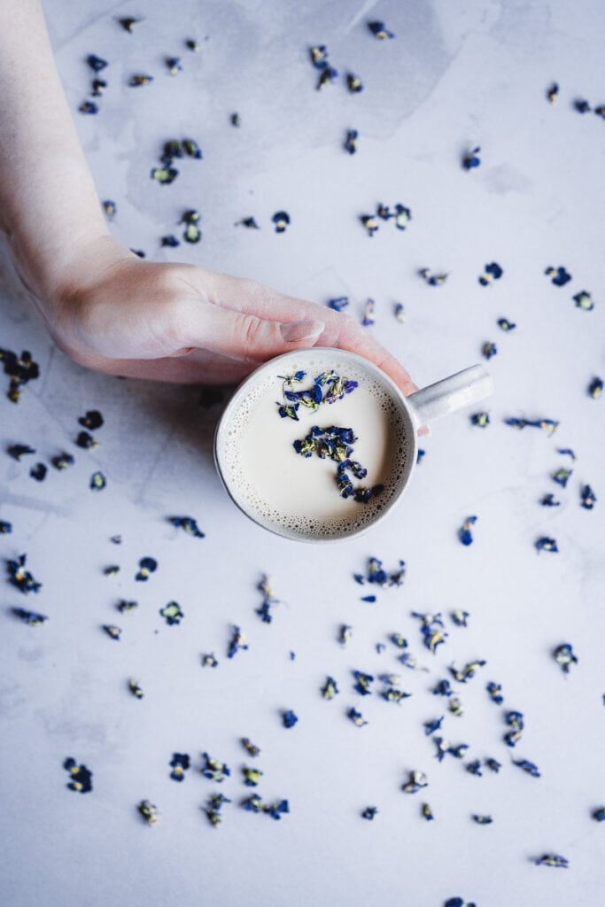 a hand holding a mug of sweet violet moon milk topped with purple dried flowers