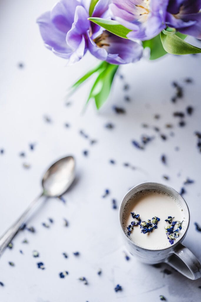a white mug of white milk topped with edible dried flower petals