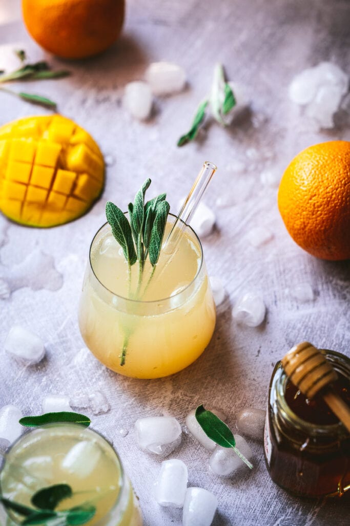 a clear glass filled with orange shrub drink and garnish with fresh sage leaves