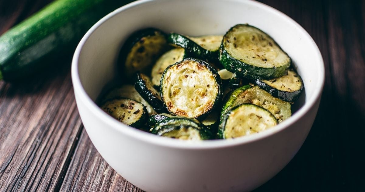 A white bowl filled with seasoned zucchini rounds.