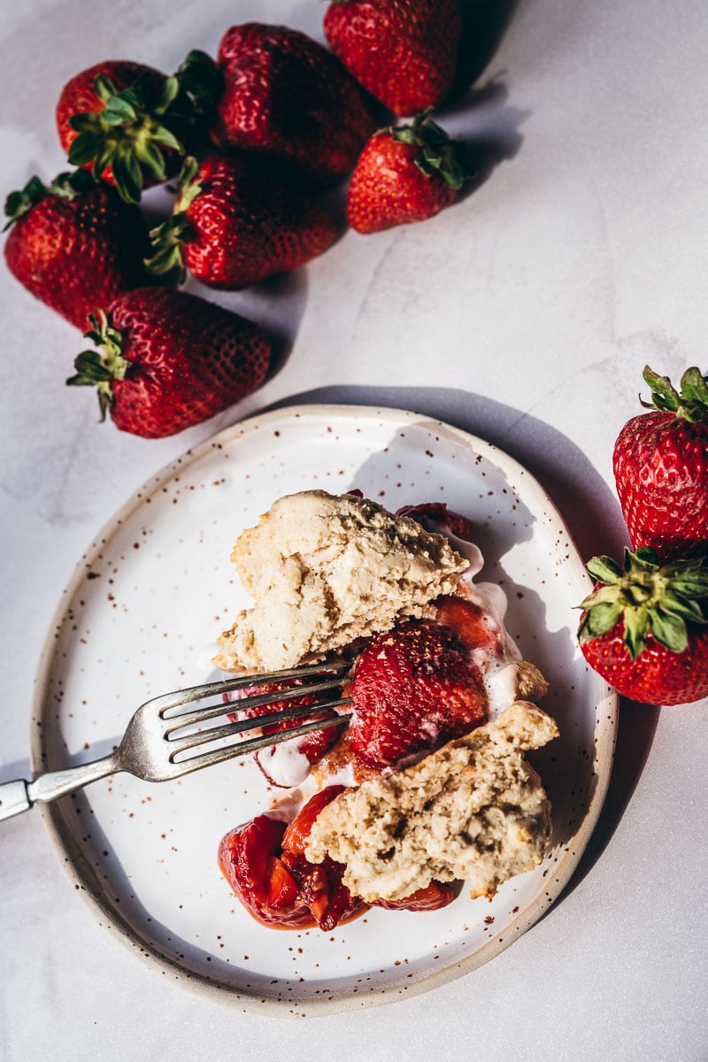 A fork pokes into the sugared strawberry topping of a strawberry shortcake dessert.