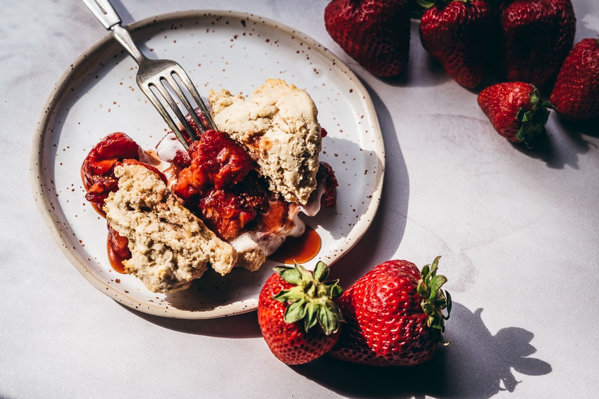 A speckled ceramic plate topped with gluten free strawberry shortcake lit by golden light.