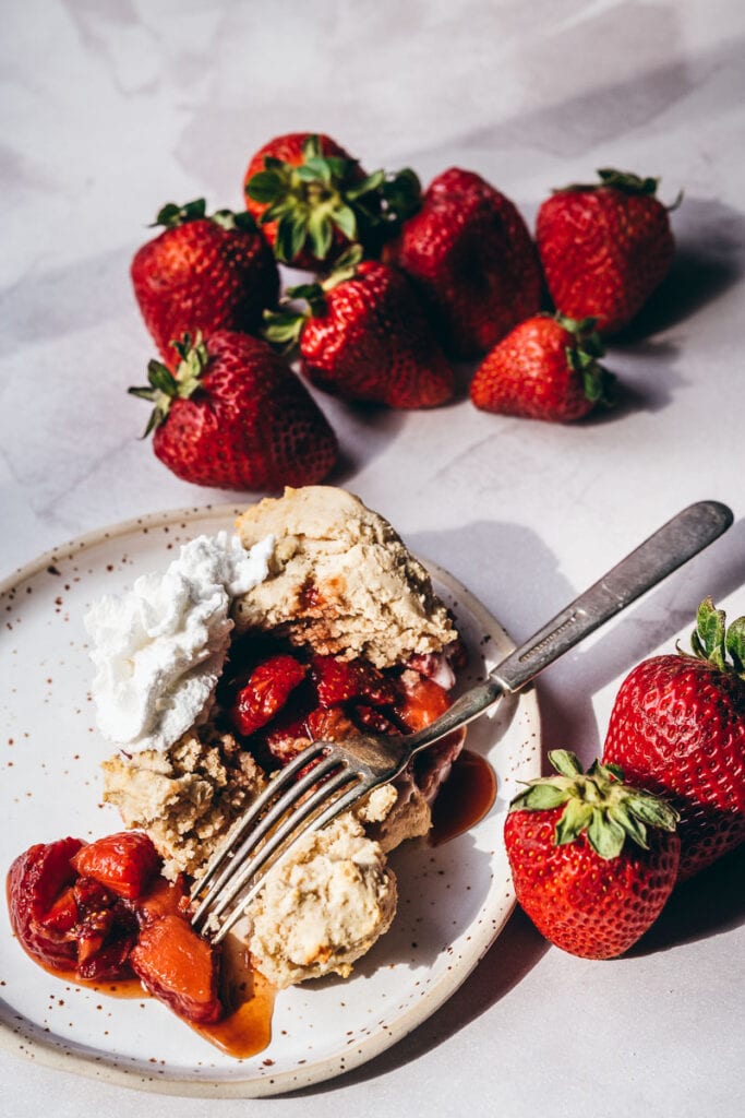 gluten free strawberry shortcake dessert lit by golden sunlight on a ceramic plate with vintage fork