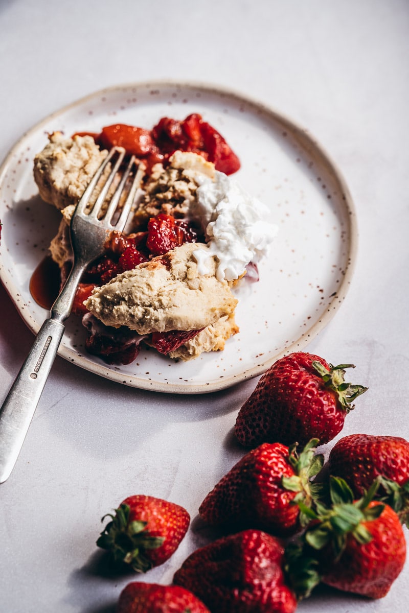 A speckled ceramic plate topped with gluten free shortcakes sugared strawberries and coconut whipped cream.