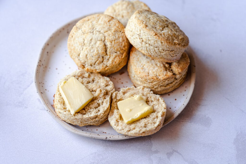 a white speckled ceramic plate topped with cut biscuits with pats of butter on top