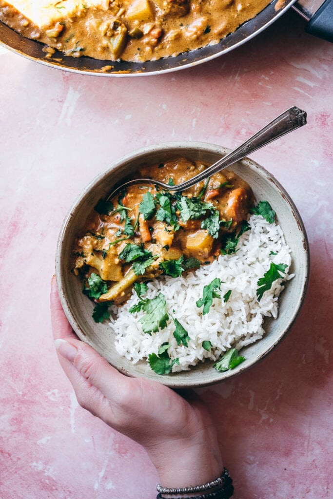 a silver spoon in a grey ceramic bowl filled with white rice and fresh veg korma