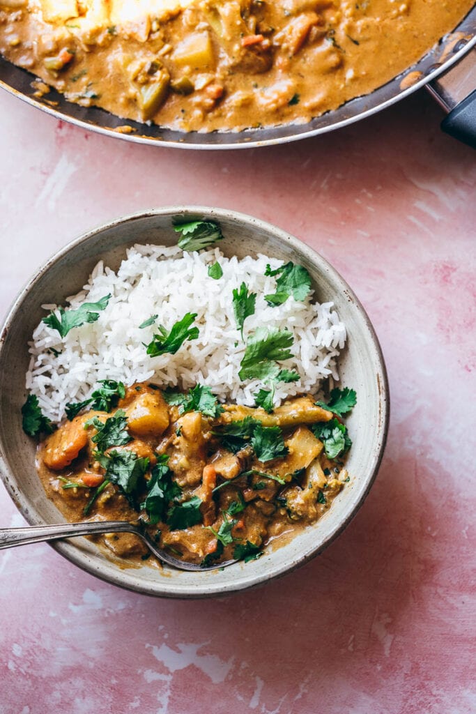 a spoon juts out of a bowl of vegan korma curry