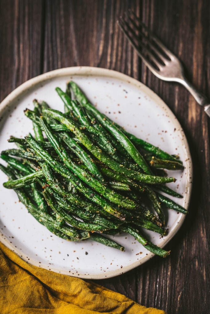 A close top view of cooked crispy green beans resting on speckled ceramic plate.