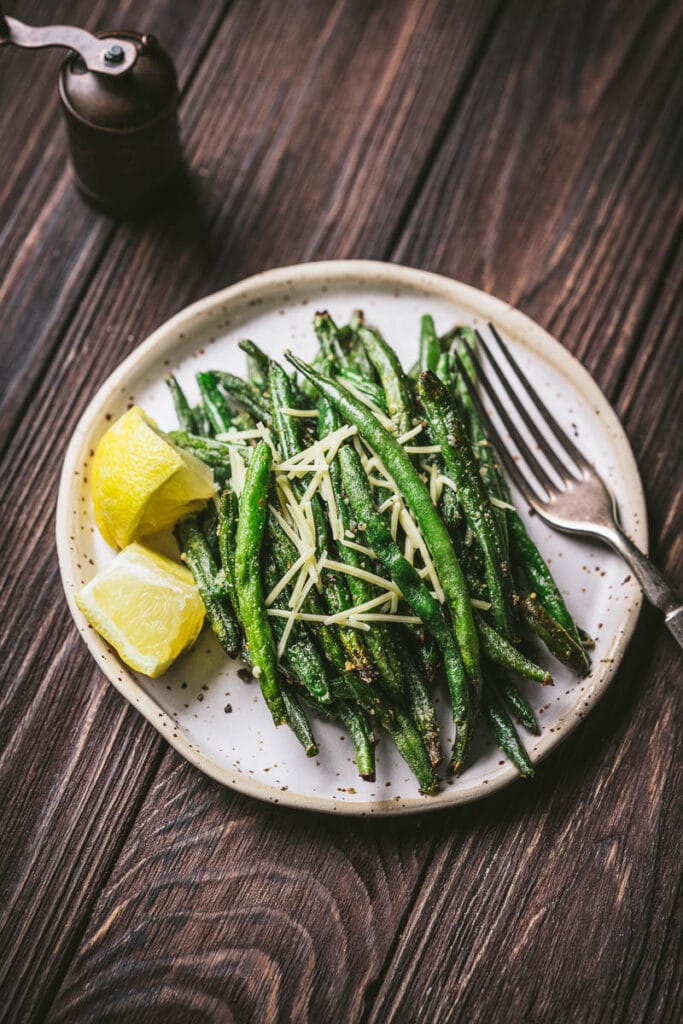 Crispy air fryer green beans garnished with lemon wedges and parmesan cheese.