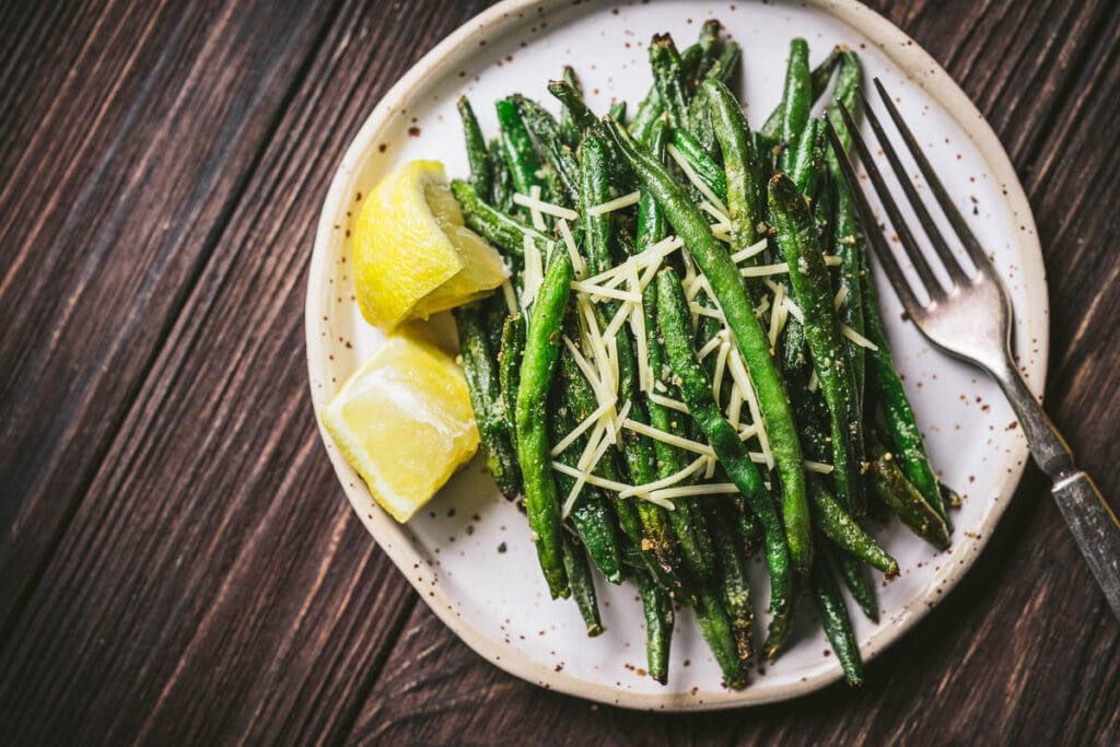 A speckled white matter ceramic plate topped green beans garnished with parmesan and lemon juice.