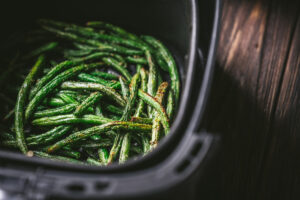 Crispy air fryer green beans served in an air fryer basket, set against a rustic wooden surface in the background.