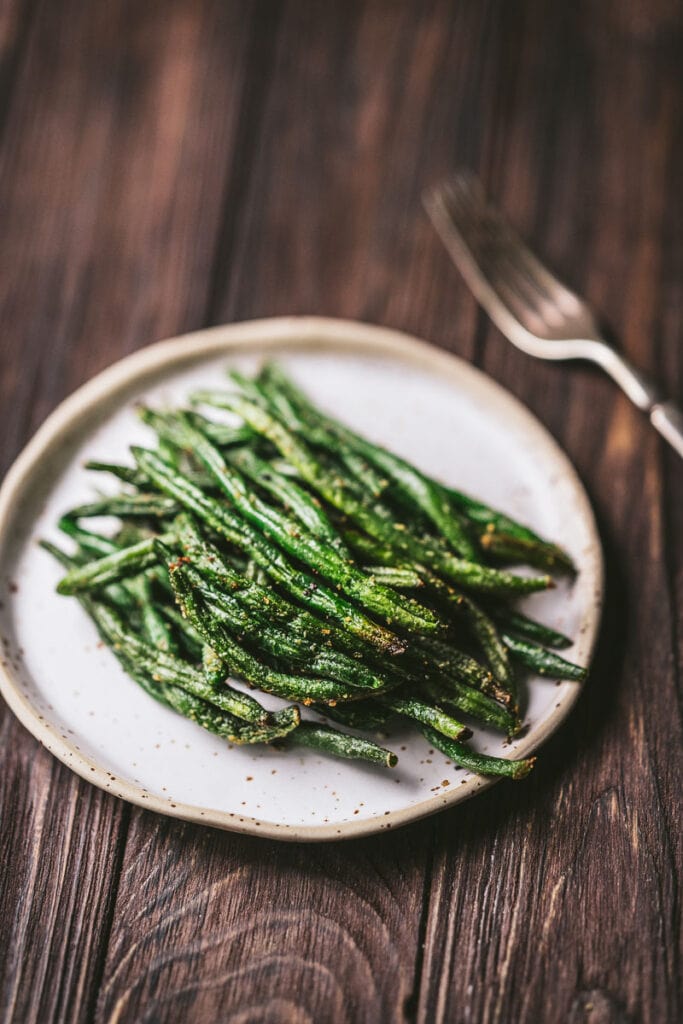 A ceramic white plate topped with crispy green beans.