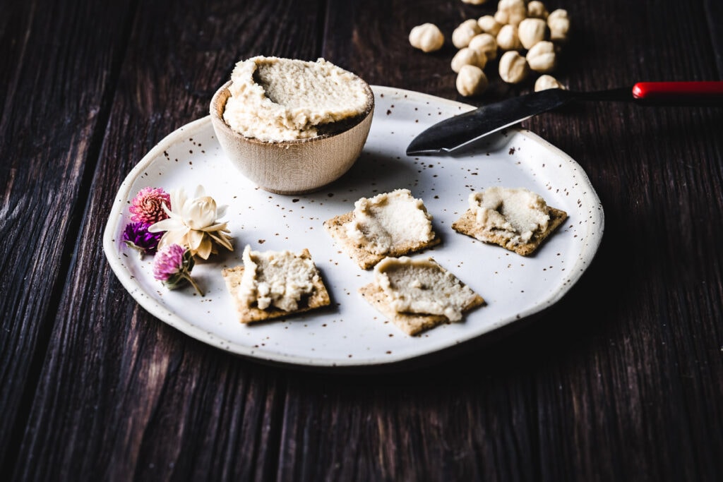a small wooden bowl of vegan cream cheese resting on a speckled ceramic plate on a wooden table