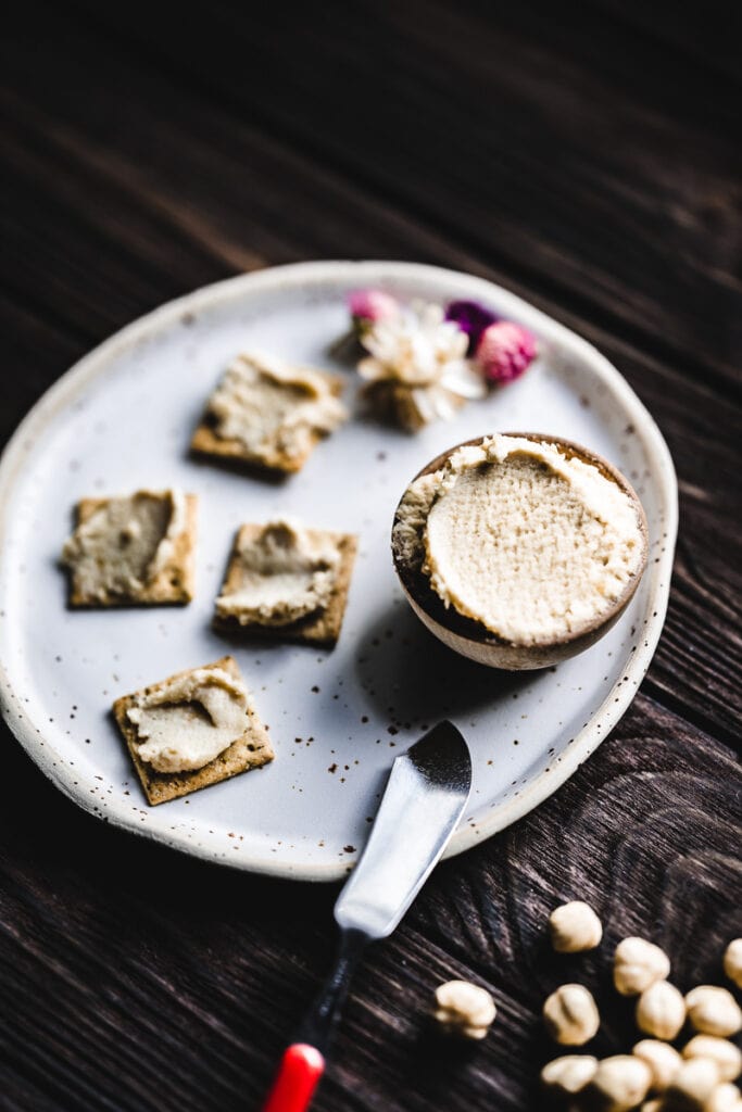 a small bowl of hazelnut spread in a small bowl and spread on crackers sitting on ceramic plate