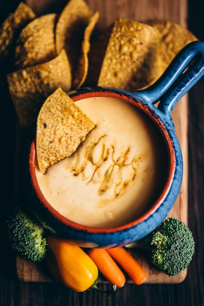 a corn tortilla chips rest in a bowl of spicy queso with ghost pepper honey drizzled on top