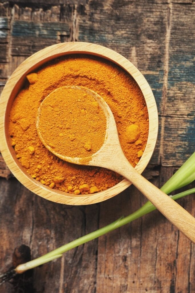 a wooden bowl filled with ground turmeric powder