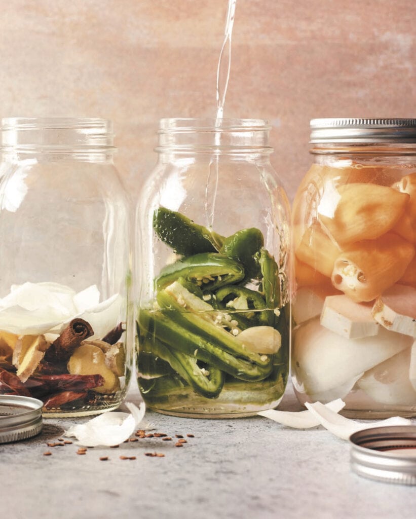 a brine being poured into a jar with jalapenos and garlic