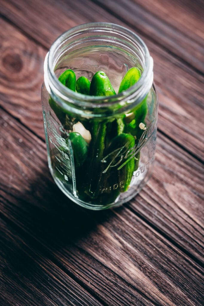 a mason jar filled with green jalapeno chiles and garlic cloves