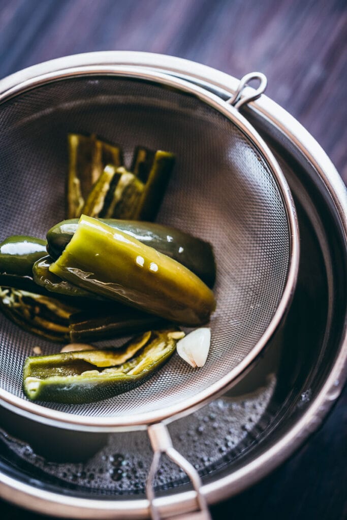 a mesh strainer filled with fermented jalapenos and garlic