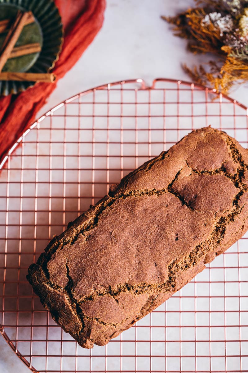 a orange brown loaf of freshly baked gluten free pumpkin bread resting on a cooling rack