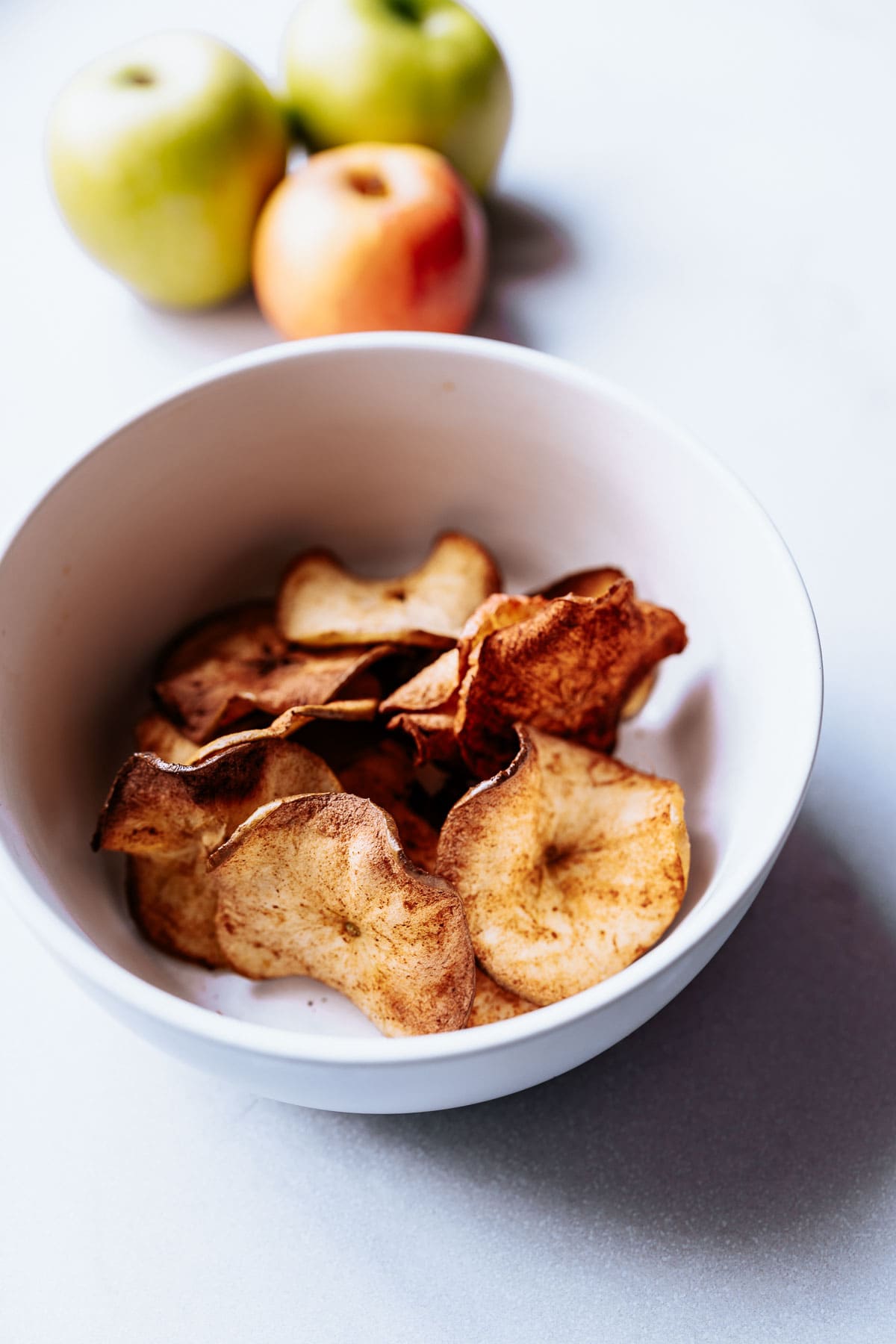 a closeup of homemade apple chips in a white bowl