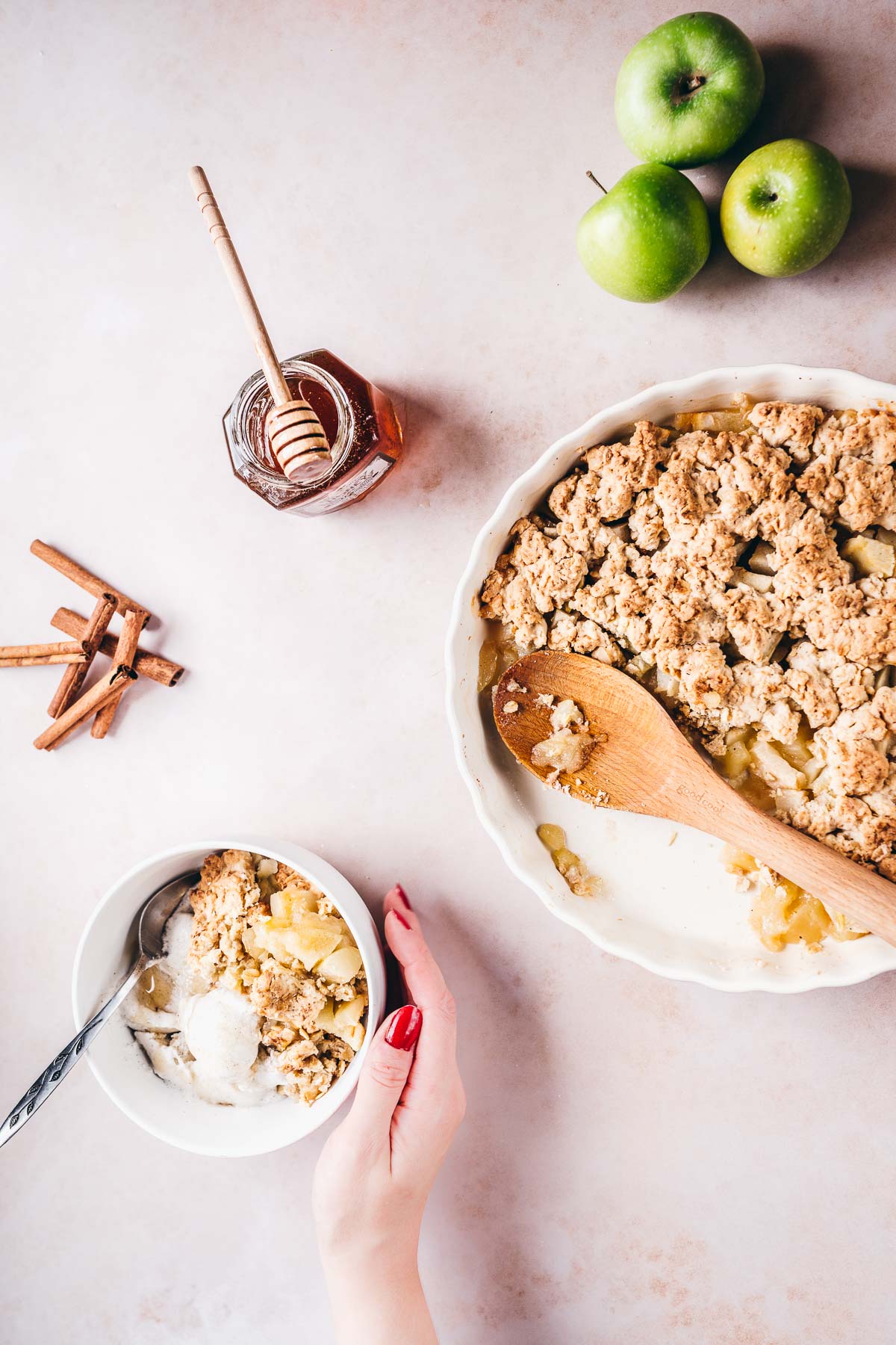 a hand cupping a white bowl filled with gluten free apple crisp made with honey and oats