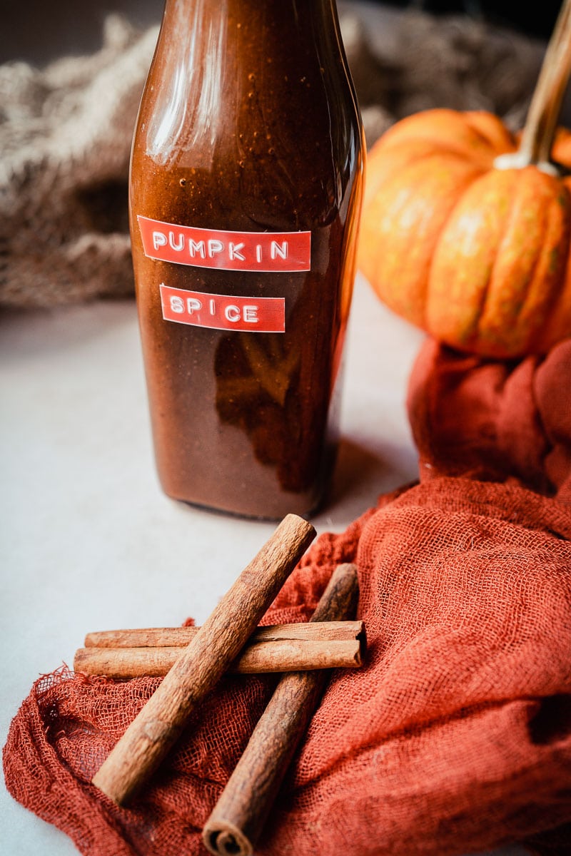 a clear bottle sitting next to cinnamon sticks and pumpkin with a orange lable that says pumpkin spice