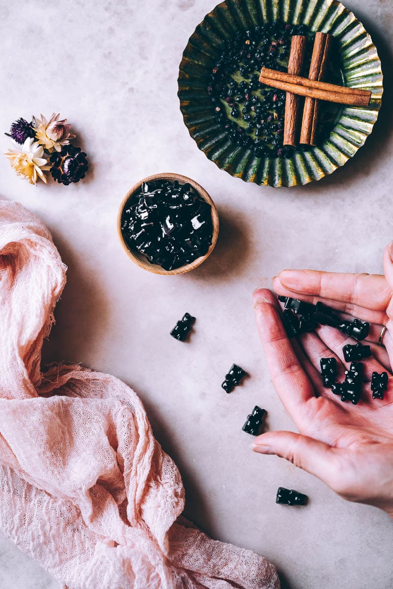 hands cupping dark purple gummy bears made with elderberry syrup