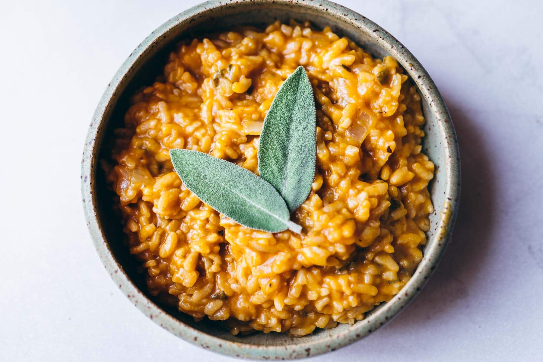 a green ceramic bowl filled with creamy pumpkin risotto topped with fresh sage leaves