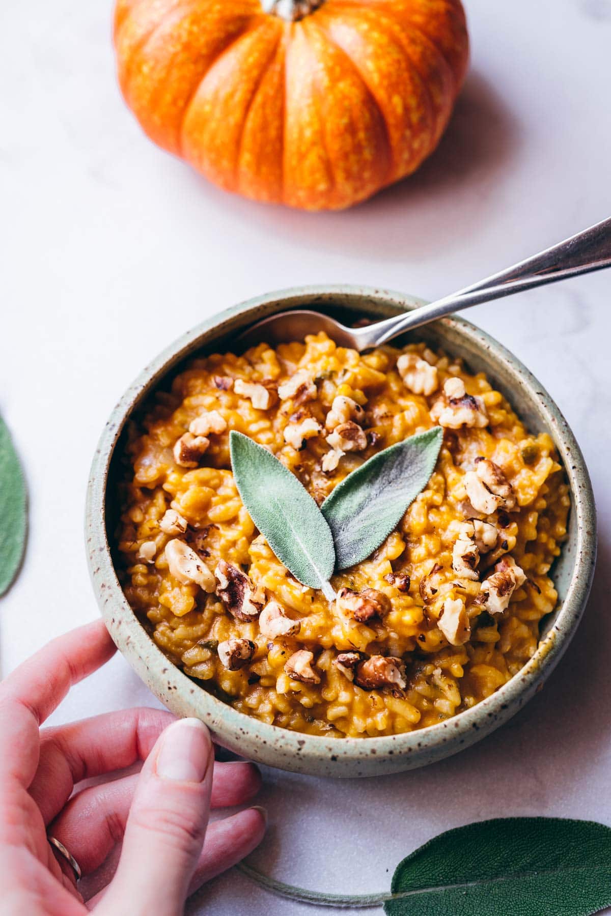 a ceramic bowl of instant pot pumpkin risotto topped with sage and toasted walnuts