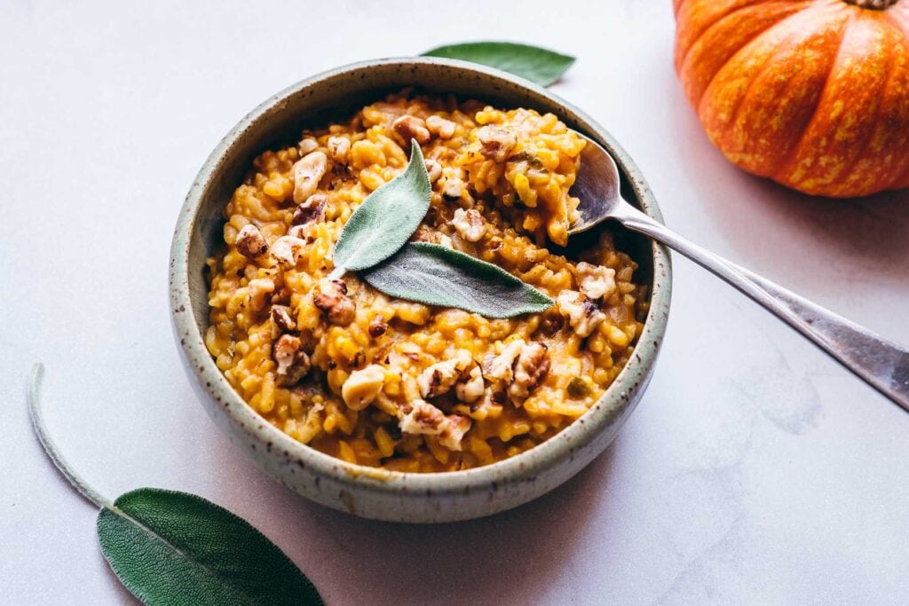 creamy instant pot sage pumpkin risotto topped with walnuts in a small green ceramic bowl
