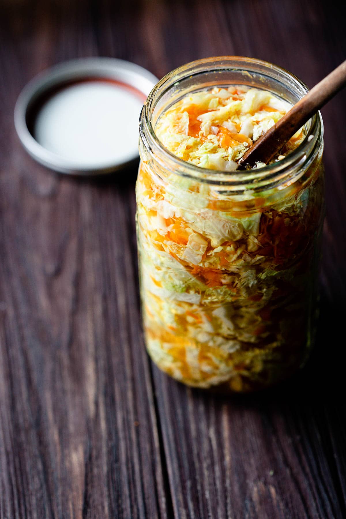 a wooden spoon is stuck into a large clear mason jar filled with pickled cabbage and carrots