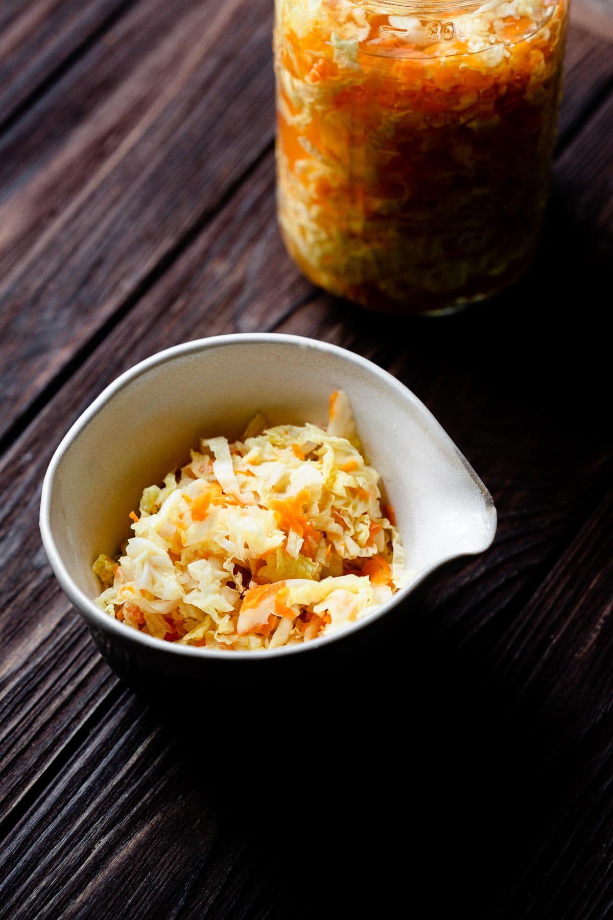 a white ceramic bowl filled with pickled cabbage carrots and garlic