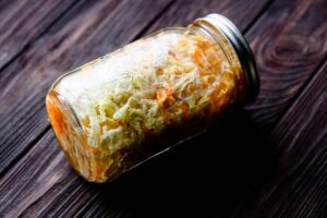 A glass jar filled with pickled cabbage and carrots, lying on its side on a dark wooden surface.