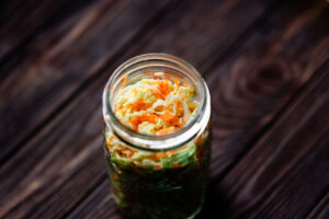 Glass jar filled with pickled cabbage and carrots, placed on a dark wooden surface.