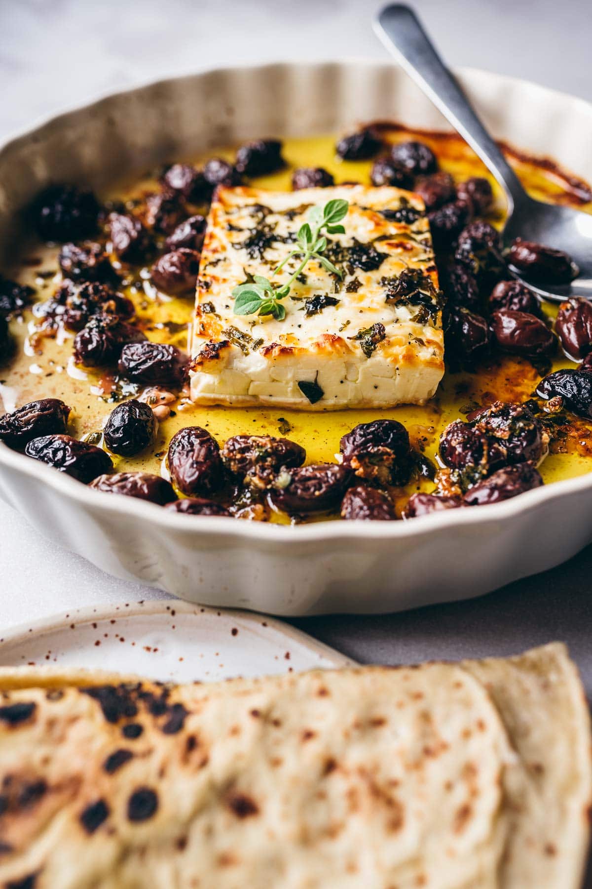 a side view of freshly baked feta cheese resting in a dish of olive oil and olives