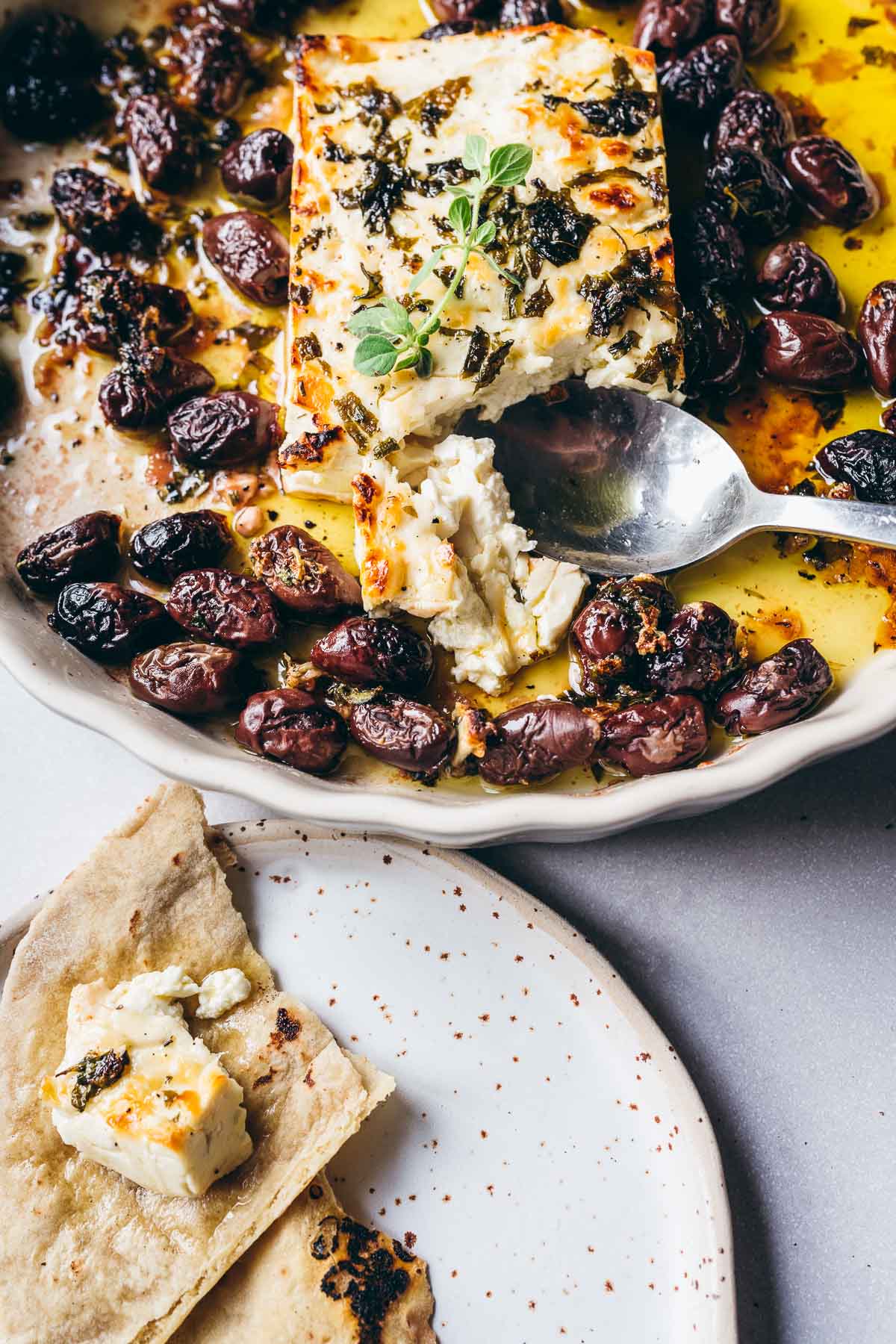 a spoon digs into freshly baked feta with herbs and olives