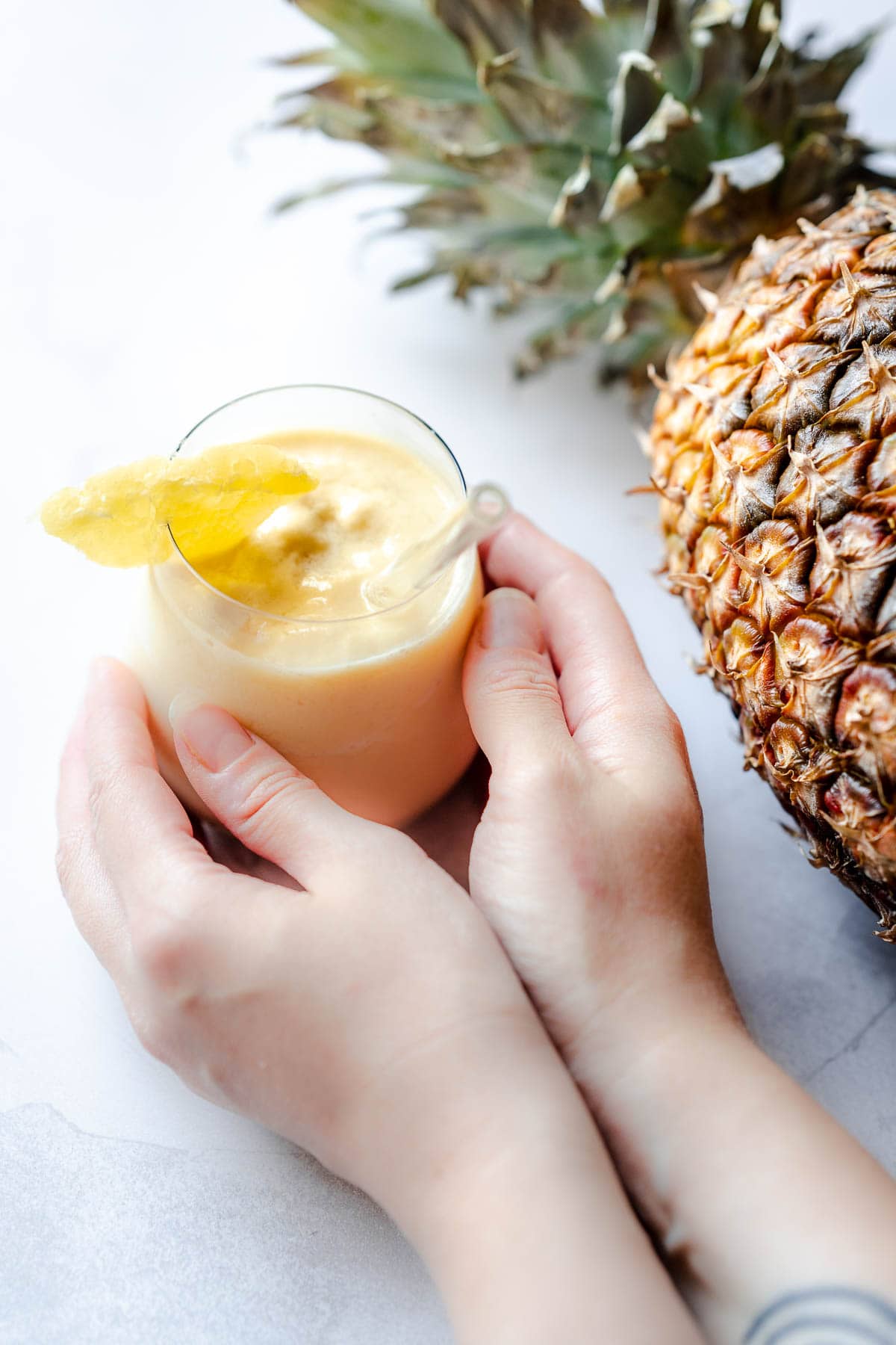 hands holding a refreshing glass of frozen pineapple smoothie