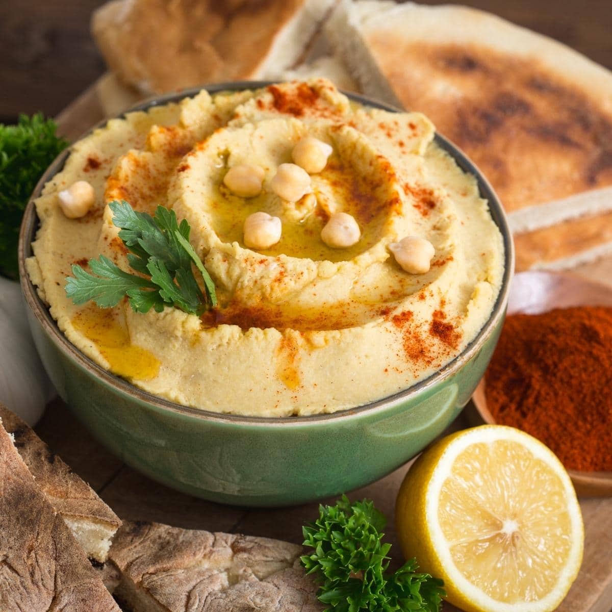 a bowl of hummus topped with chickpeas, olive oil, paprika and parsley.