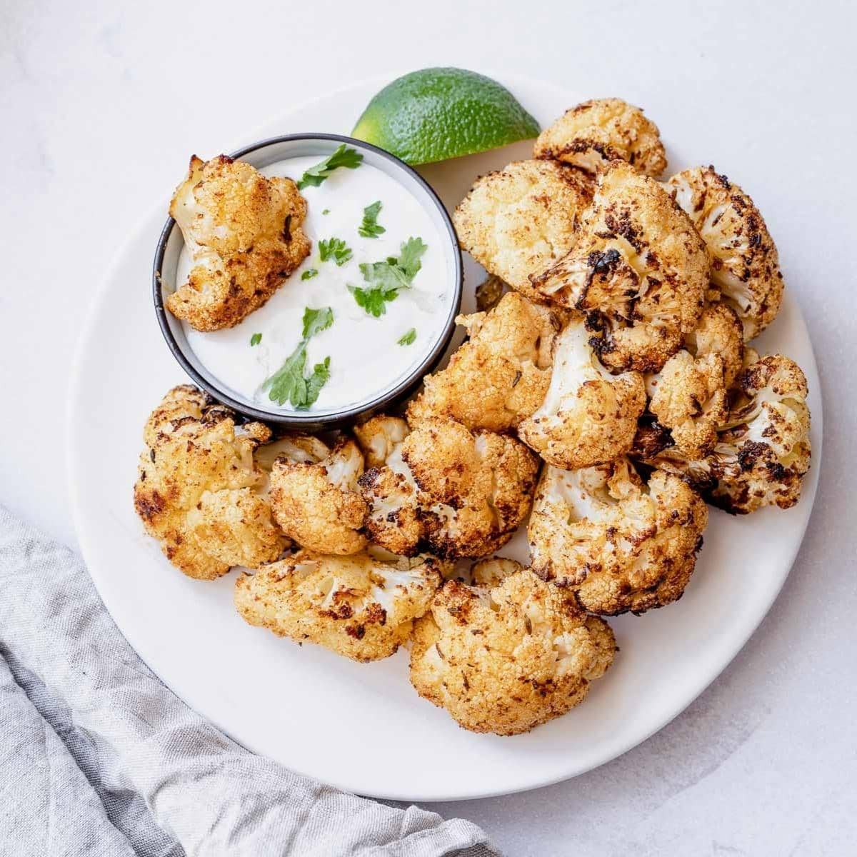 a white plate topped with crispy air fried cauliflower with a side of lime yogurt