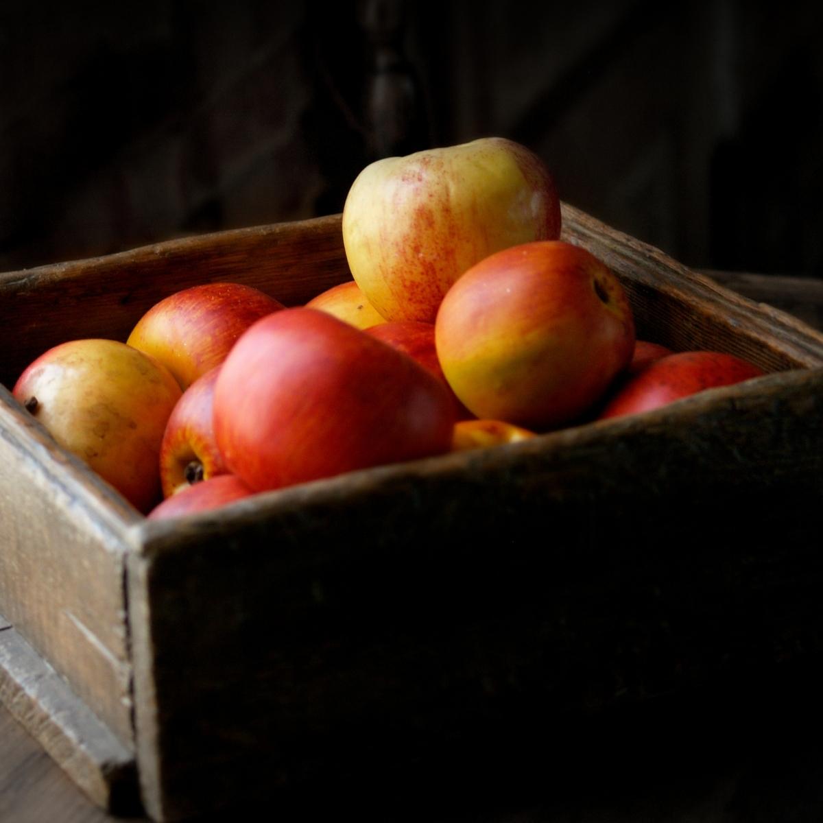 a moody photography of red apples in a wood box.