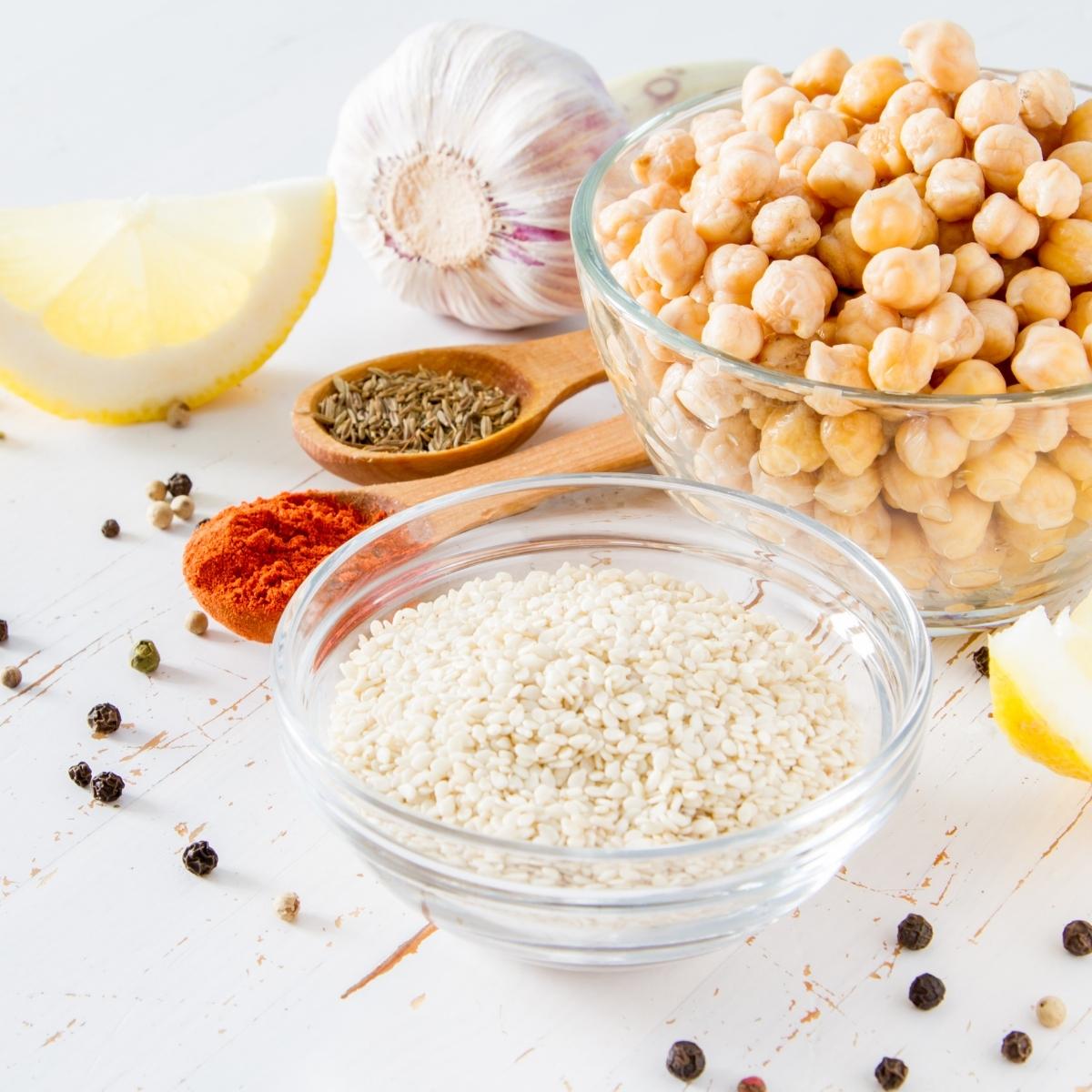 bowls of hummus ingredients including sesame seed tahini, chickpeas, cumin seeds, paprika, pepper, lemon juice and garlic.