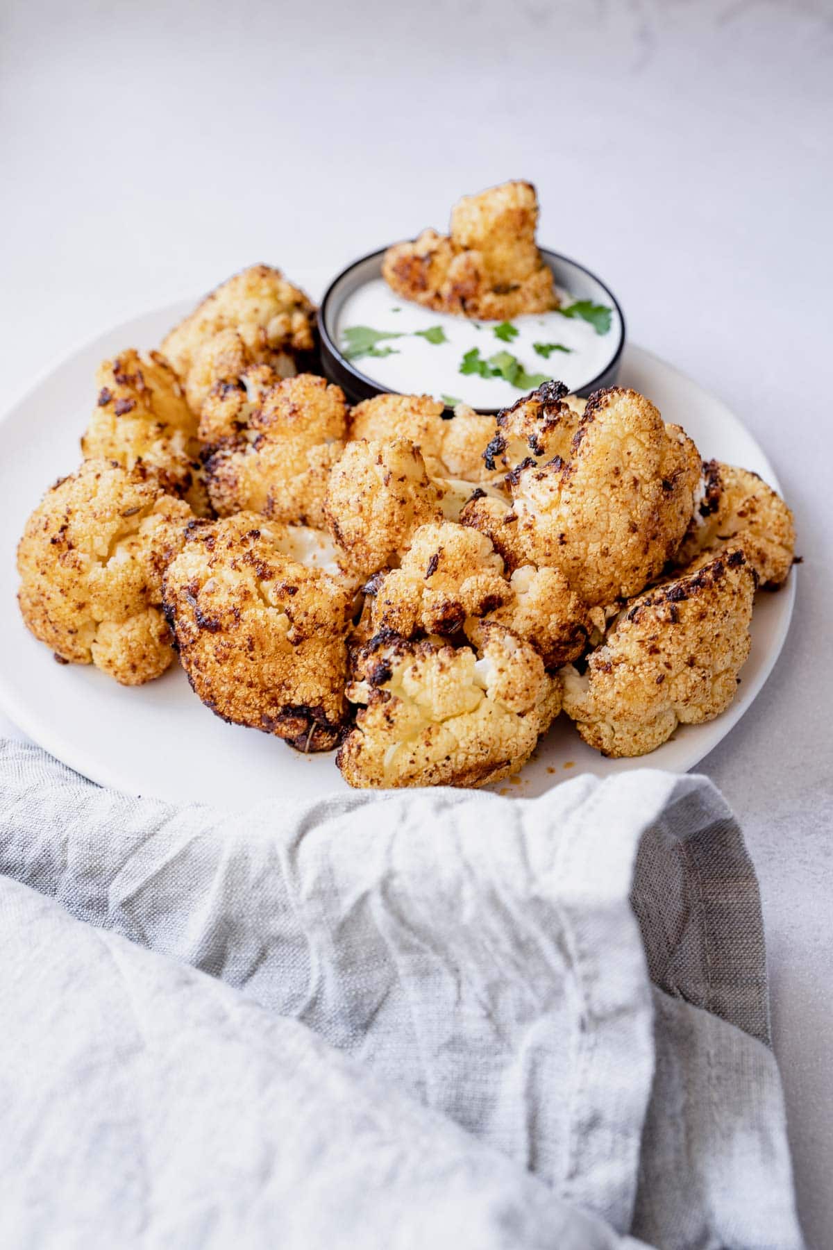 A close up shot of crispy spiced air fried cauliflower florets resting on white ceramic plate.