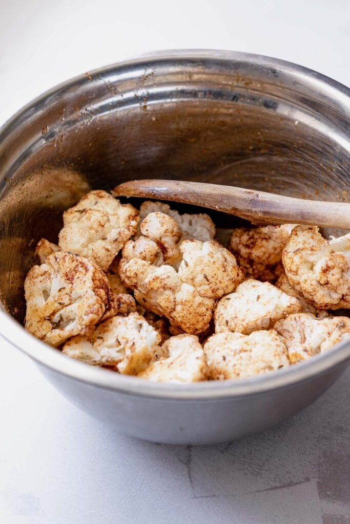 A mixing bowl of raw cauliflower coated in spices.